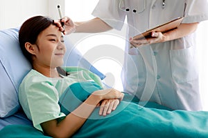 Asian pretty female patient lying on bed in hospital and smiling with happiness while doctor checking her health and report the