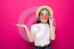 Asian pretty woman with open hand palm in sunglasses and straw hat isolated on pink background