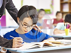 Asian primary school student getting help from teacher