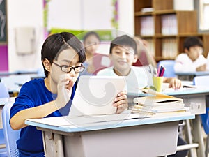 Asian primary school student using tablet in classroom