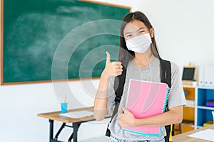 Asian primary student girl thumb up and  wearing masks to prevent the outbreak of Covid 19 in classroom while back to school