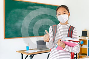 Asian primary student girl thumb up and  wearing masks to prevent the outbreak of Covid 19 in classroom while back to school