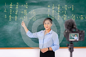 Asian primary teacher tutor explaining math in blackboard giving remote school class online lesson teaching looking at camera in