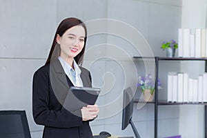 Asian professional business young woman in black suit smiles happily stand with confidence and look at the camera while she works