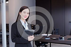 Asian professional business young woman in black suit smiles happily stand with confidence and look at the camera while she works