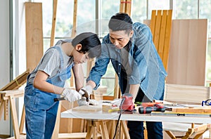 Asian professional carpenter engineer dad teaching young boy son in jeans outfit with gloves safety goggles nailing steel hammer