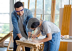 Asian professional carpenter engineer dad teaching young boy son in jeans outfit with gloves safety goggles nailing steel hammer