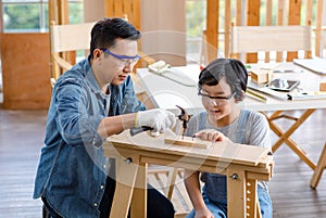 Asian professional carpenter engineer dad teaching young boy son in jeans outfit with gloves safety goggles nailing steel hammer