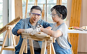 Asian professional carpenter engineer dad teaching young boy son in jeans outfit with gloves safety goggles nailing steel hammer