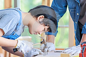 Asian professional carpenter engineer dad teaching young boy son in jeans outfit with gloves safety goggles nailing steel hammer