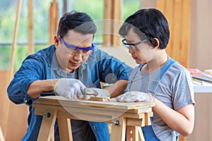 Asian professional carpenter engineer dad teaching young boy son in jeans outfit with gloves safety goggles nailing steel hammer