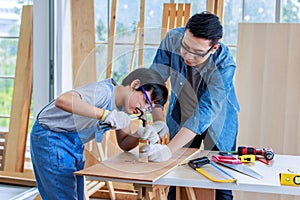 Asian professional carpenter engineer dad teaching young boy son in jeans outfit with gloves safety goggles nailing steel hammer