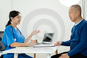 Asian professional female doctor talking with male patient about his pain and symptoms while giving consultation at table