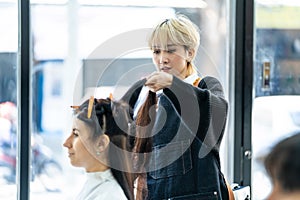 Asian professional female stylist cutting woman`s hair in salon. The woman hairdresser using scissors cut the young girl sitting i