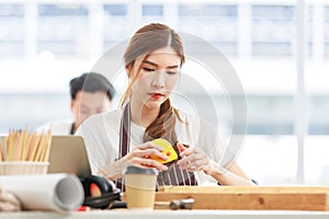 Asian professional focused female carpenter worker staff in apron sitting holding using measuring tape measure wooden sticks on