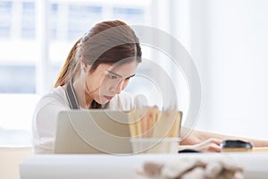 Asian professional focused female carpenter worker staff in apron sitting holding using measuring tape measure wooden sticks on