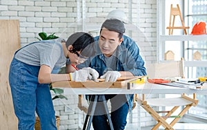 Asian professional male carpenter woodworker engineer dad in jeans outfit with safety gloves and goggles helping teaching young