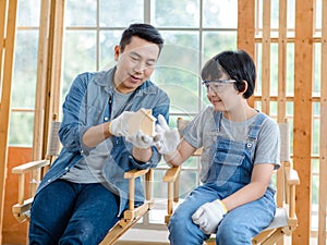 Asian professional male carpenter woodworker engineer dad in jeans outfit with safety gloves and goggles helping teaching young