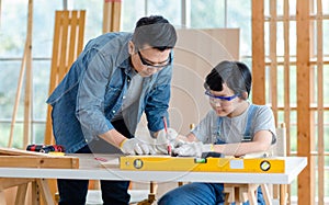 Asian professional male carpenter woodworker engineer dad in jeans outfit with safety gloves and goggles helping teaching young