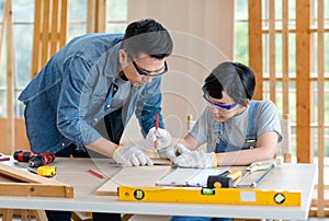 Asian professional male carpenter woodworker engineer dad in jeans outfit with safety gloves and goggles helping teaching young