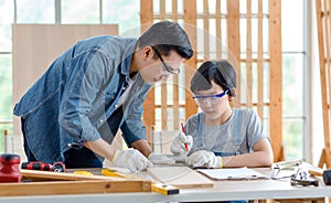 Asian professional male carpenter woodworker engineer dad in jeans outfit with safety gloves and goggles helping teaching young