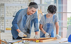 Asian professional male carpenter woodworker engineer dad in jeans outfit with safety gloves and goggles helping teaching young