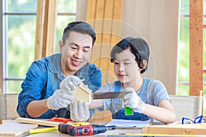 Asian professional male carpenter woodworker engineer dad in jeans outfit with safety gloves holding small home model teaching