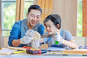 Asian professional male carpenter woodworker engineer dad in jeans outfit with safety gloves holding small home model teaching