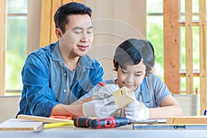 Asian professional male carpenter woodworker engineer dad in jeans outfit with safety gloves holding small home model teaching
