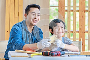 Asian professional male carpenter woodworker engineer dad in jeans outfit with safety gloves holding small home model teaching