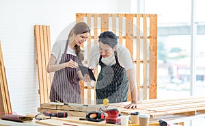 Asian professional male and female carpenter worker lover couple in apron standing smiling helping looking at short notes on paper