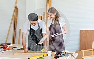 Asian professional male and female lover couple carpenter worker in apron using measuring tape measure wooden sticks on workbench