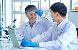 Asian professional mature male scientist teacher in white lab coat and rubber gloves sit smiling teaching science student using