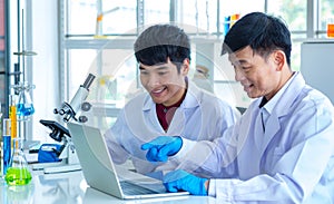 Asian professional mature male scientist teacher in white lab coat and rubber gloves sit smiling teaching science student using