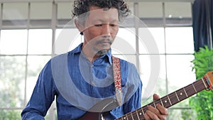 Asian professional musician playing electric guitar in music practice room.