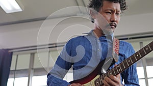 Asian professional musician playing electric guitar in music practice room.
