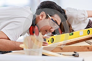 Asian professional skilled male carpenter worker staff in apron with earphones and safety goggles standing using water level gauge