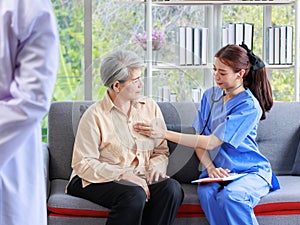 Asian professional successful female internship nurse in blue uniform sitting on sofa couch smiling using stethoscope listening to