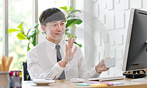 Asian professional successful male businessman employee in formal shirt with necktie sitting hold coffee cup waving hand greeting