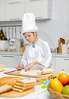 Asian professional young little boy pastry chef in white cooking uniform and tall cook hat standing using heart shape mold cutting