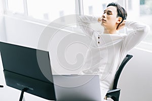 Asian programmer sits with his head back in his chair to relax after a tiring working time photo