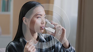 Asian race woman take drug remedy drinking glass of still water indoors at home. Korean pregnant sick girl holding pill