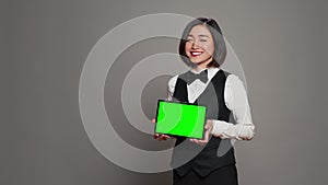 Asian receptionist holding tablet with greenscreen on camera,