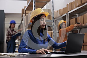 Asian retail storehouse employee analyzing orders checklist on laptop