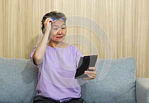 Asian retired elderly with eyeglasses, sitting on the sofa watching at tablet computer. With presbyopia syndrome she cannot focus