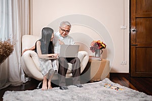 Asian retirement grandfather and pretty granddaughter watching e-book for learning to education together by tablet and laptop.