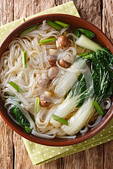 Asian rice noodle soup with mushrooms and bok choy closeup in a bowl. Vertical top view