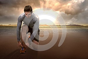 Asian runner man tying running shoelaces on the beach