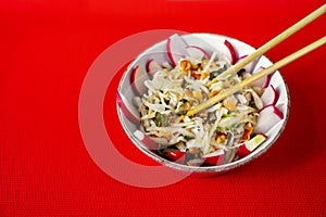 Asian salad in bowl with chopsticks on red background