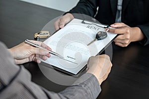 Asian salesman holding rental contract and hand over car key to client while he is holding pen to signing